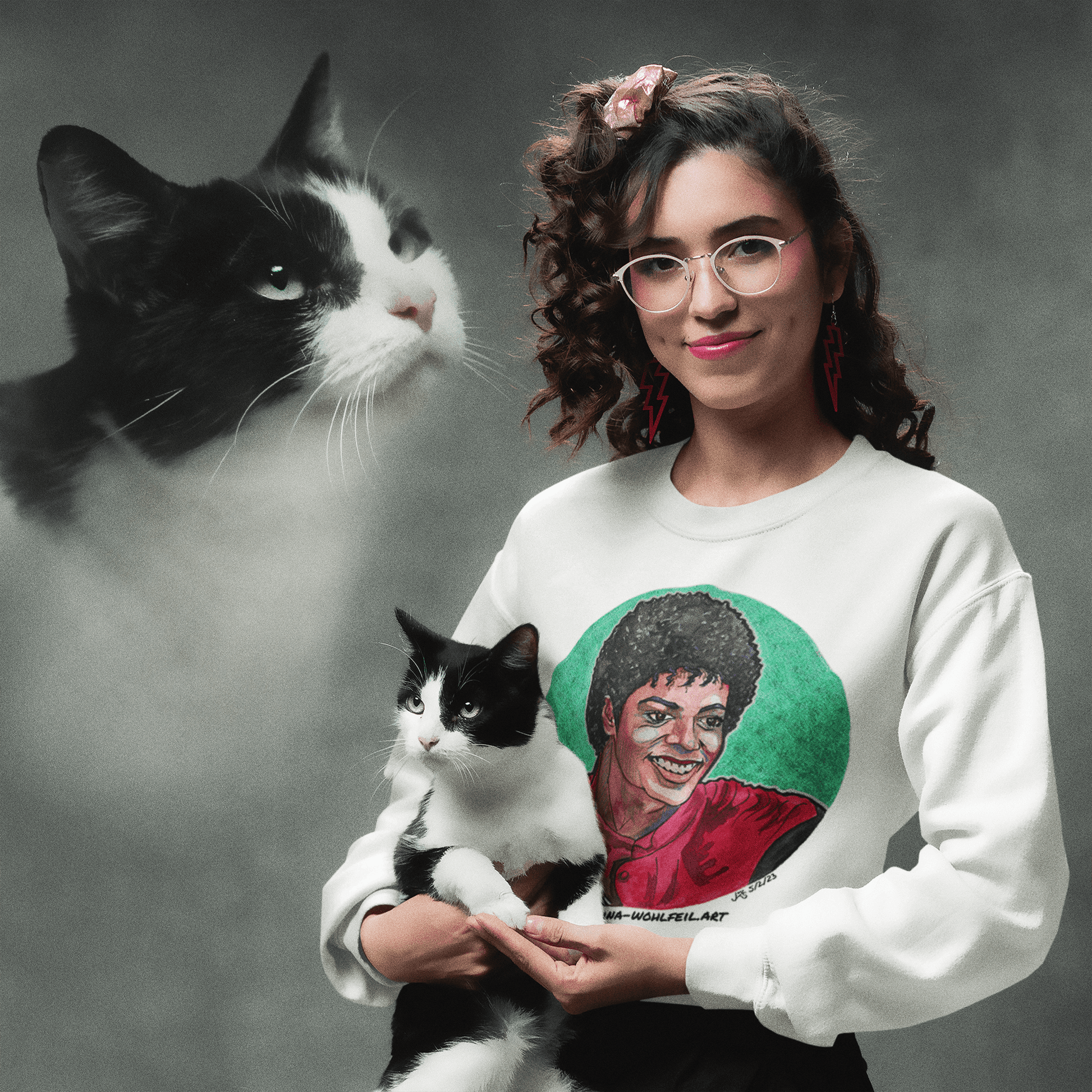 Frau in klassischem Unisex-Sweatshirt mit Michael Jackson Comic-Skizze, tüddelt schwarz-weiße Katze, mit größerem Bild der Katze im Hintergrund.